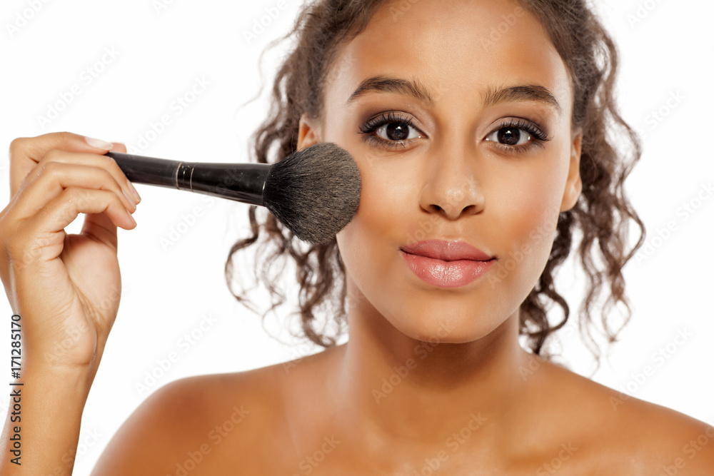 a young dark skinned woman applies a highlighter on her face a young dark skinned woman applies a highlighter on her face