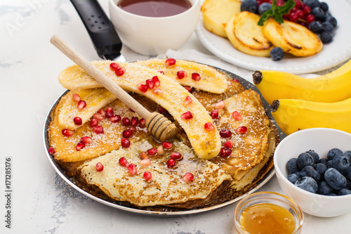 Sweet crepes with banana, honey and pomegranate seeds in a frying pan. Delicious family breakfast concept. Space for text photo