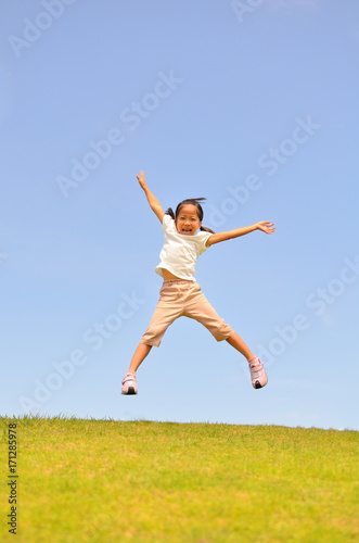 芝生広場でジャンプする女の子（青空）