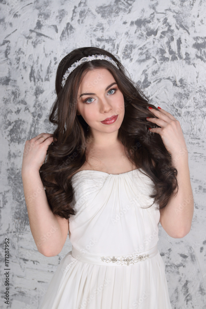 Fototapeta premium Pretty young brunette in diadem and with hairdo poses in white studio