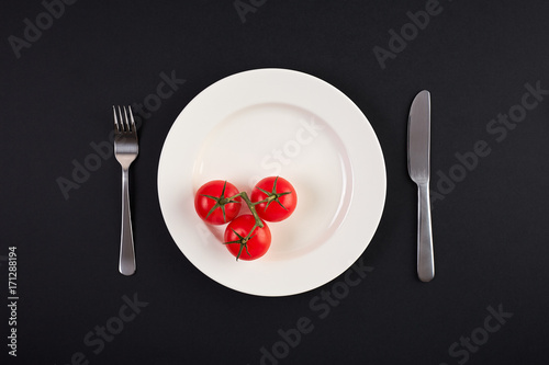 Top view of white dish with tomato on background of black table