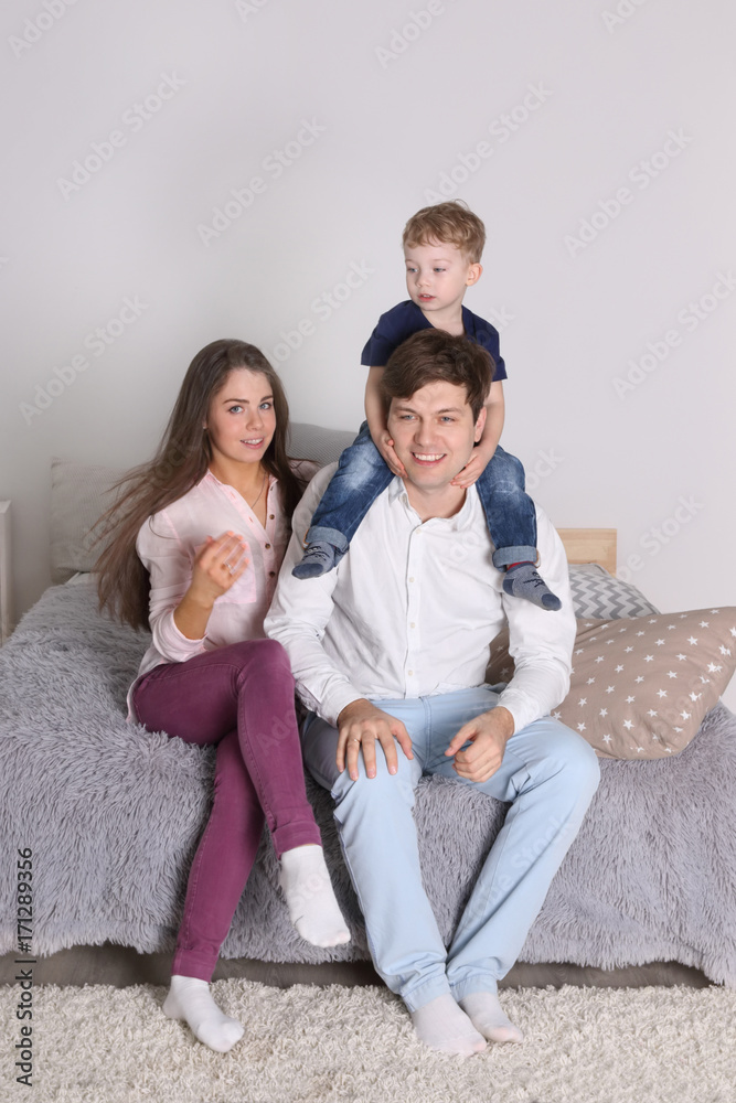 Happy father, mother and little son sit on bed in bedroom at home