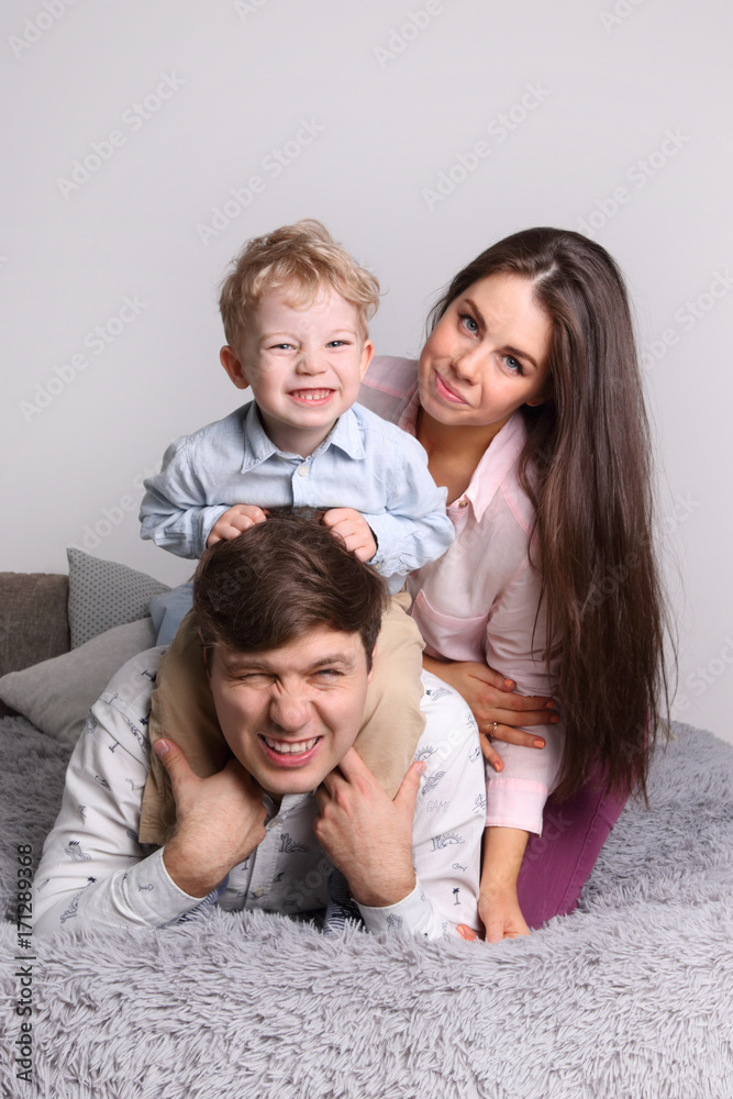 Happy father, mother, little son lies on grey bed in cozy bedroom Happy father, mother, little son lies on grey bed in cozy bedroom