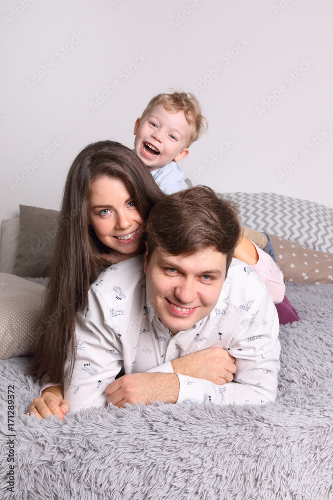 Happy young father, mother, little son lies on bed in bedroom