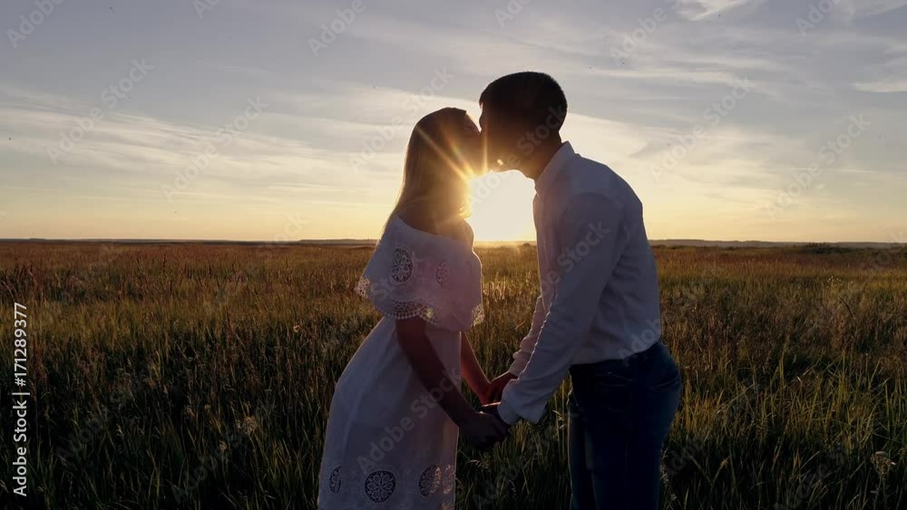 Young beautiful couple in a wheat field. Silhouette on sunset background. Slow motion Young beautiful couple in a wheat field. Silhouette on sunset background. Slow motion