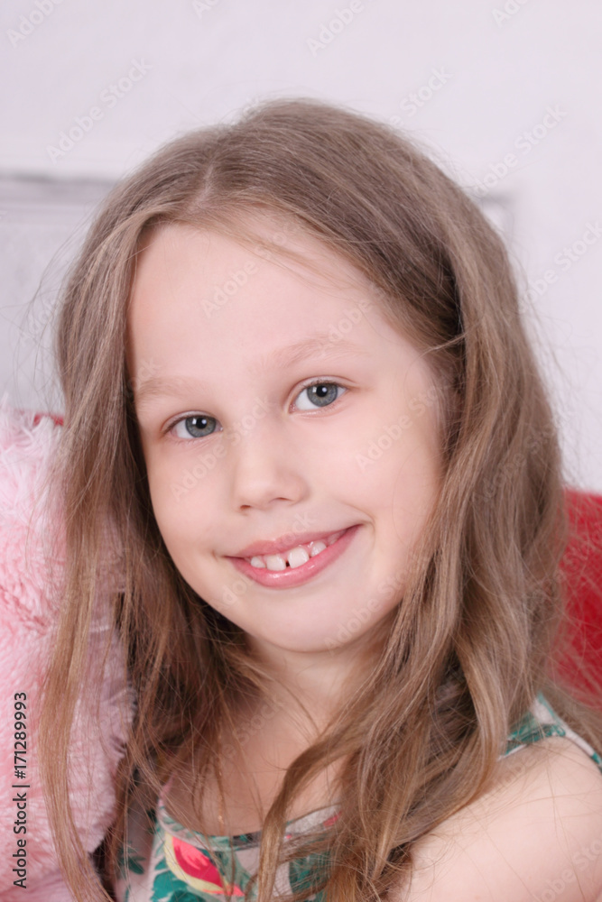 Happy little girl in armchair smiles in white room at home, close up portraiit Happy little girl in armchair smiles in white room at home, close up portraiit