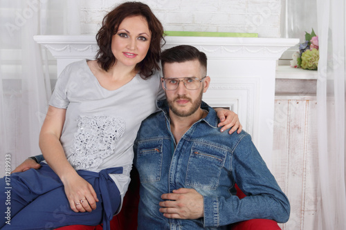 Handsome man in glasses sits in armchair, woman embraces he in white room