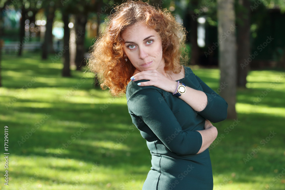 Curly young woman in dress poses among trees in summer green garden Curly young woman in dress poses among trees in summer green garden