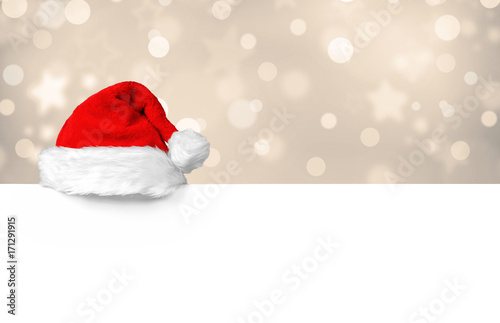 Weihnachtsmütze auf weißer Plakatwand vor goldig schimmernden Bokeh