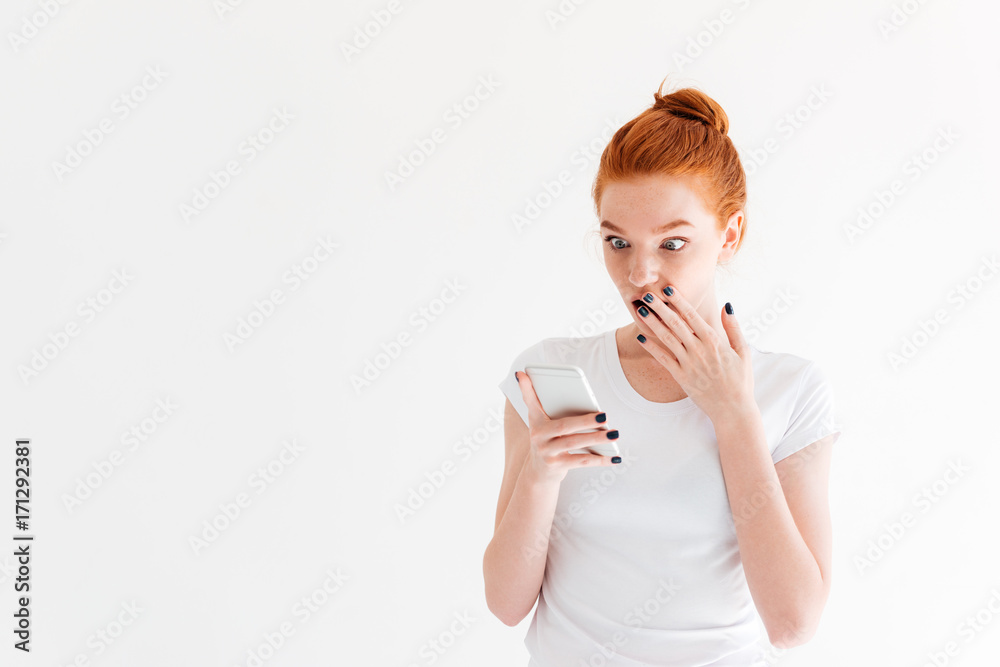 Surprised ginger woman in t-shirt using her smartphone Surprised ginger woman in t-shirt using her smartphone