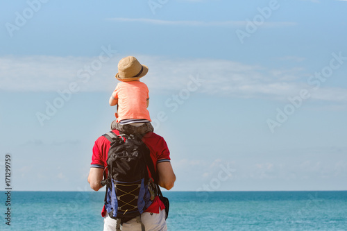 Father and son on their shoulders stand on the sea shore, rear view
