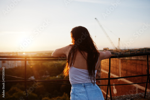 Portrait of a gorgeous young woman in casual clothing admiring the sunset from the roof of a building.