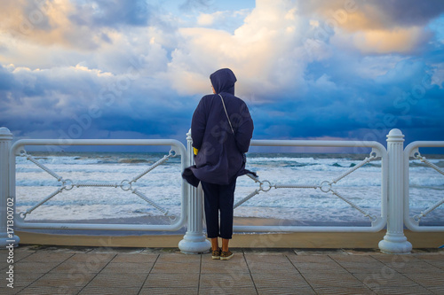Mujer de espalda mira al mar como se acerca la tormenta junto a la valla del paseo de la playa