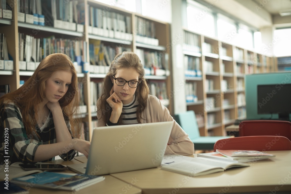 Female friends using laptop in library Female friends using laptop in library