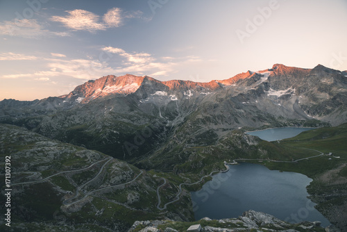 High altitude alpine lake  dams and water basins in idyllic land with majestic rocky mountain peaks glowing at sunset. Wide angle view on the Alps.