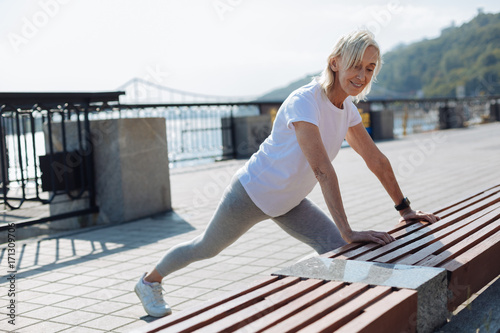 Slender senior woman stretching near bench