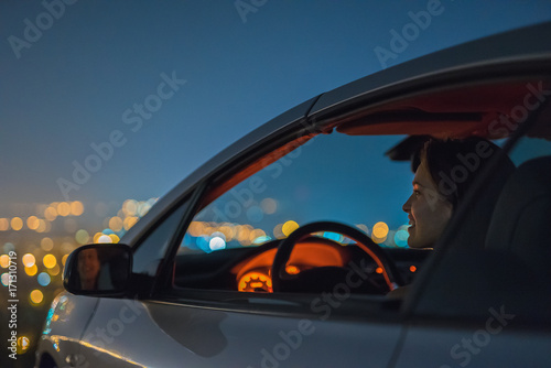 The attractive woman sit in the car on the background of the city. night time