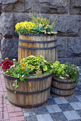 деревянные бочки с травой и цветами у каменной стены