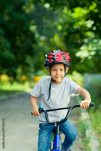 Little boy learns to ride a bike in the Park near the home. Portrait of a cute kid on bicycle. Happy smiling child in helmet riding a cycling.
