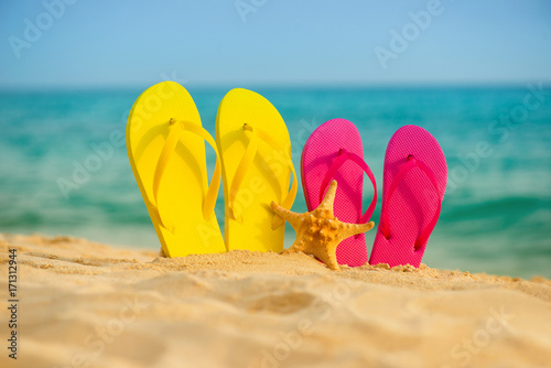 Sea-stars with yellow and pink sandals stand in the sand against the background of the sea.