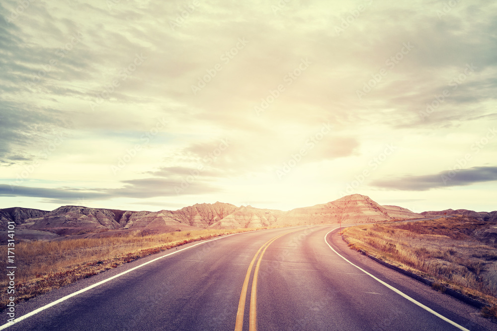 Fototapeta premium Vintage toned picturesque road in Badlands National Park at sunset, travel concept background, South Dakota, USA.