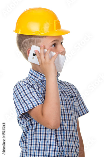Cute builder boy speaks by phone, wearing yellow protectie helmet and blue checkered shirt. White background. photo