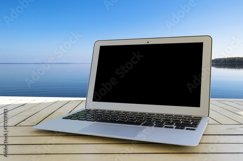 Laptop computer on wooden table. Front ocean view. Tropical island background. Open blank laptop computer empty space. Front view with copy space.