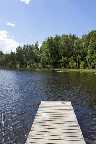 Wooden pier at the lakeside in Finland. Vivid green forest in the background with blue sky and some clouds.