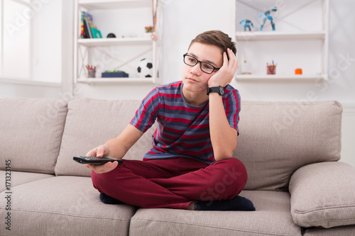 Boy watching tv and looking bored on couch at home photo