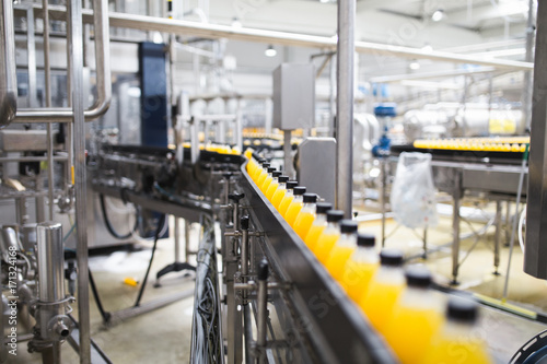 Industrial factory indoors and machinery. Robotic factory line for processing and bottling of soda and orange juice bottles. Selective focus. Short depth of field.