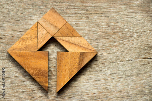 Tangram puzzle in square shape with the arrow symbol inside on wood background photo
