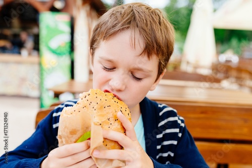 Hungry child eating burger outdoors.