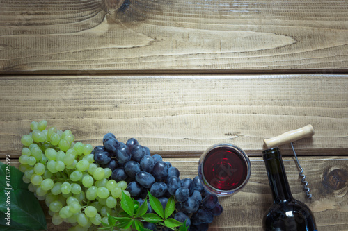 Open bottle of red wine with a glass, corkscrew and ripe grape on a wooden background. Copy space and top view.