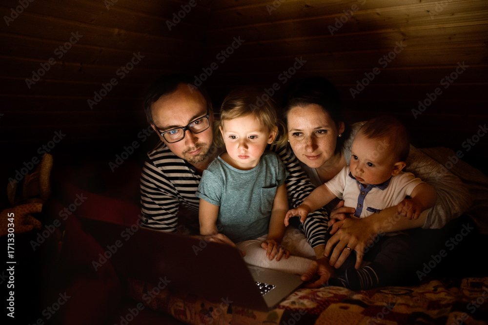 Fototapeta premium Young parents with little children and laptop at night.