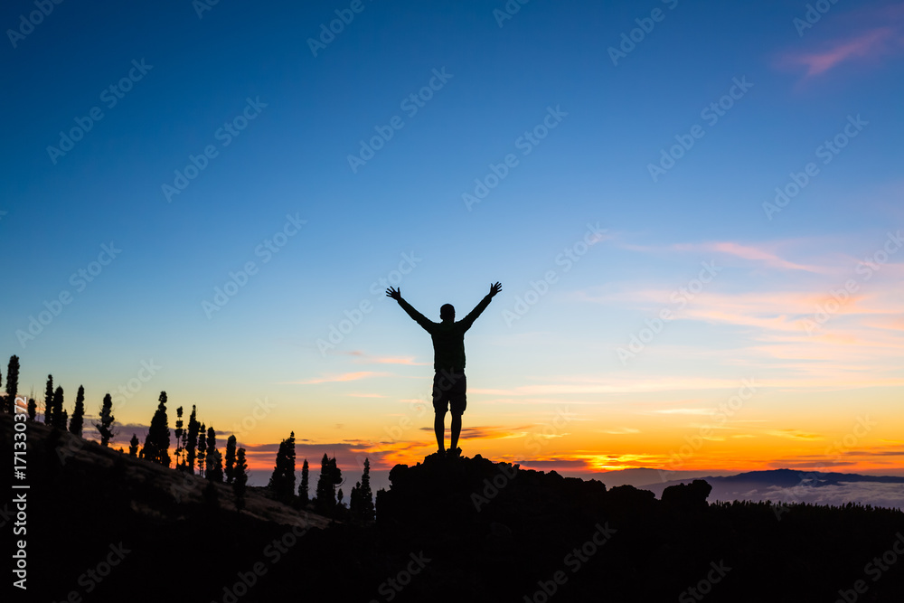 Man celebrating sunset with arms outstretched in mountains