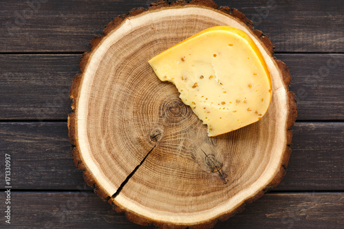 Fototapeta Naklejka Na Ścianę i Meble -  Piece of gouda herb cheese on natural wood disc