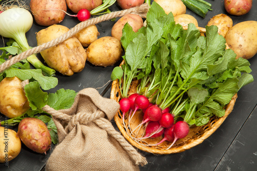 Fresh vegetables, radishes and potatoes on a black wooden background