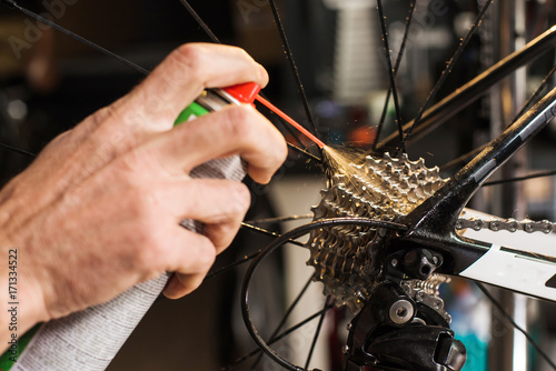 Male hands cleaning and oiling a bicycle chain and gear with oil spray