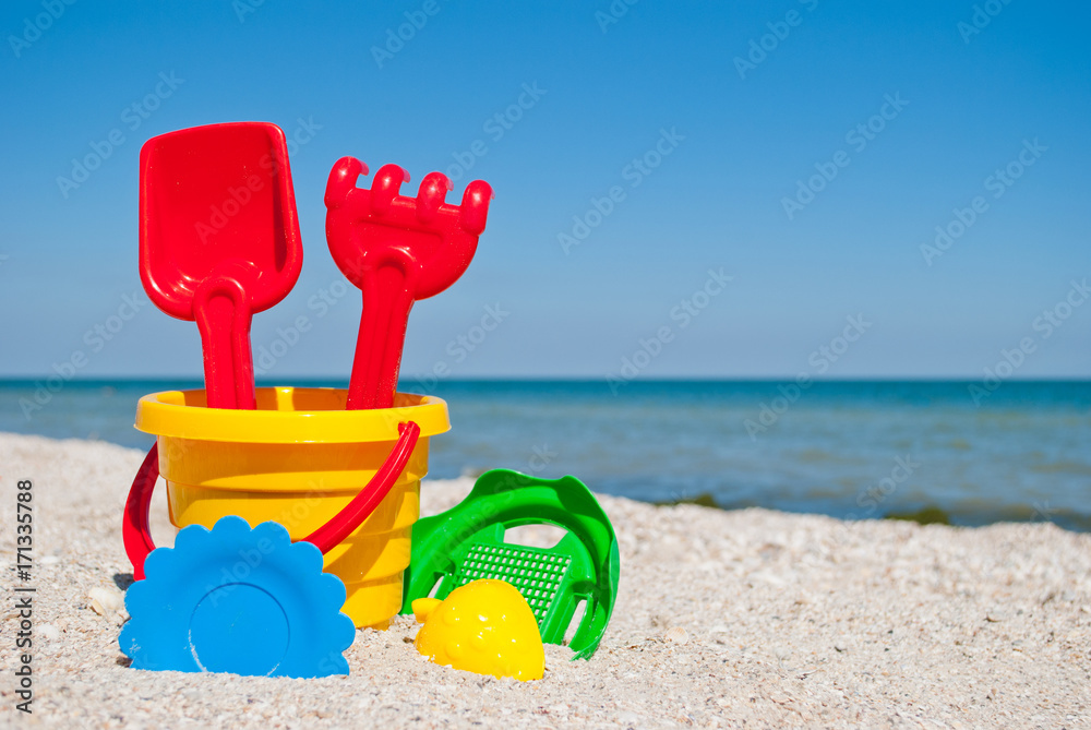 Yellow baby bucket with red handle, plastic red spatula and rake, green sieve, yellow sand form of strawberry, blue plate, blue sea and sky, yellow sand beach seashells seaside summer vacation sunny Yellow baby bucket with red handle, plastic red spatula and rake, green sieve, yellow sand form of strawberry, blue plate, blue sea and sky, yellow sand beach seashells seaside summer vacation sunny