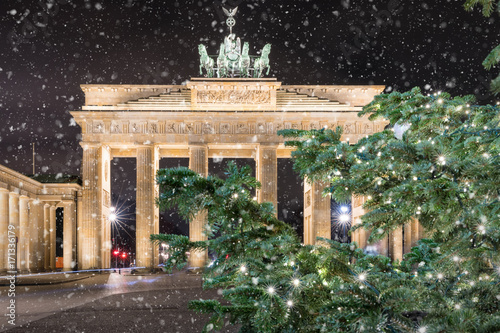 Das Brandeburger Tor in Berlin bei Nacht mit weihnachtlichem Tannenzweig und Schneefall
