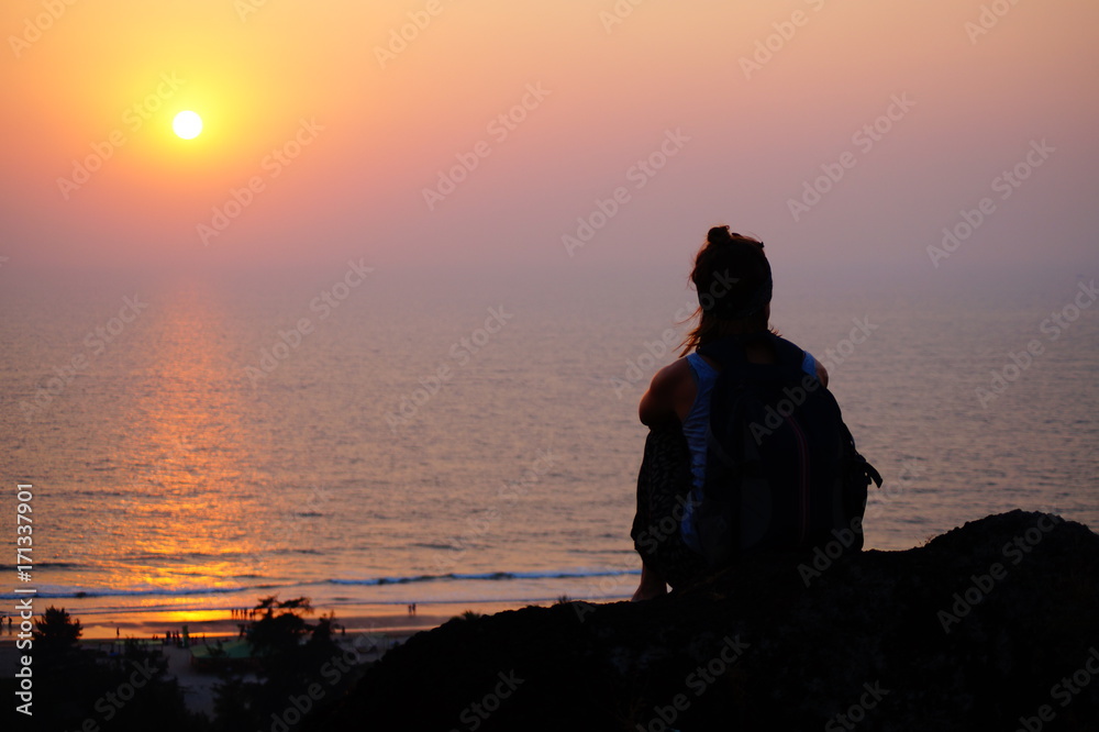 Girl sitting on the edge of the hill, sunset time, sea view