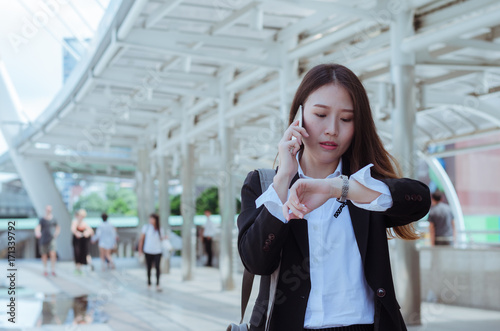 businesswoman  beautiful Asian young woman talking on mobile phone and serious look at the watch for the time.
