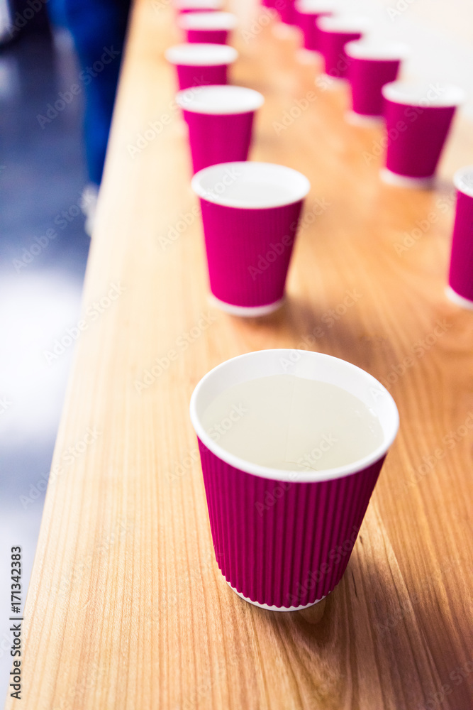 A row of the disposable paper cups with water on the wooden table. Time break during the conference, session, meeting, cup testing, or coffee cupping.