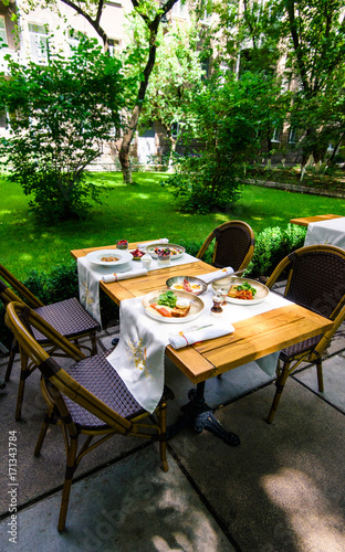 Delicious luxury breakfast or lunch with healthy food in the summer lounge zone in a restaurant or hotel. Breakfast in the garden concept. Table set for four people.