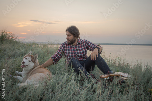 young handsome men in fields with guitar and husky dog during sunset in lake   © serejkakovalev