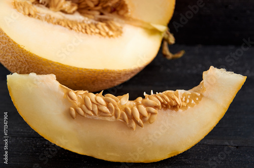 Fresh sweet yellow melon sliced on wooden black table. A piece of raw organic melon on wooden dark surface close up