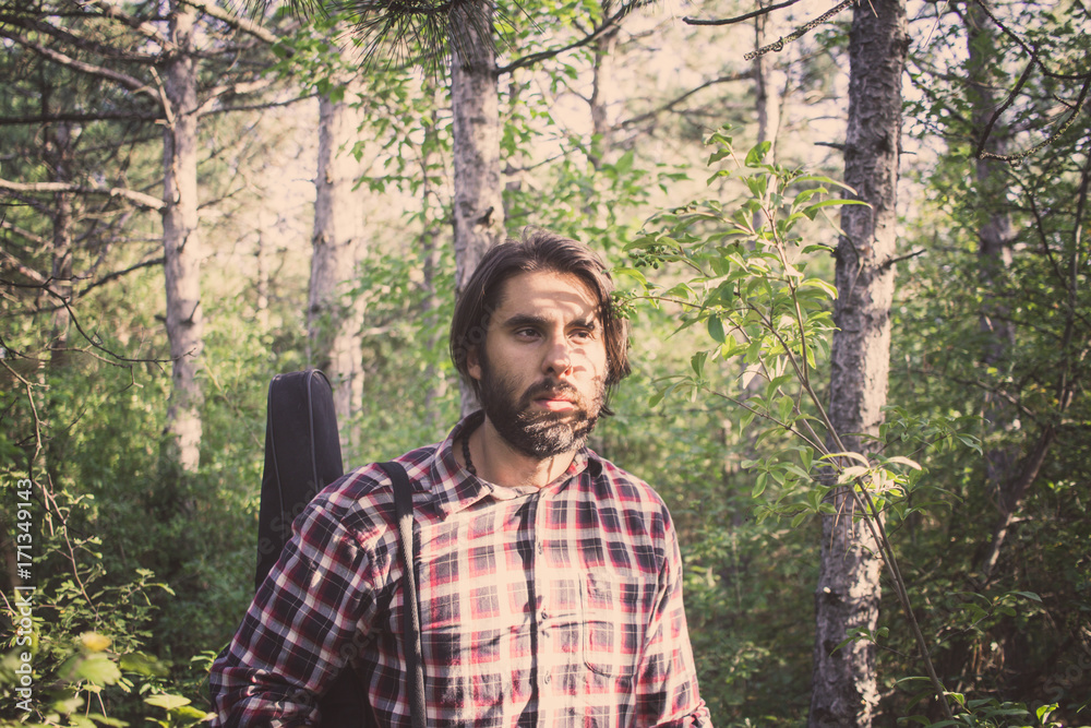 handsome male with beard and long hair walking in the summer forest with guitar case handsome male with beard and long hair walking in the summer forest with guitar case