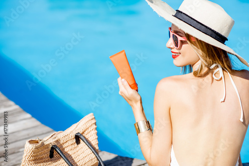 Woman in sunhat sitting with sunscreen lotion near the basin with blue water. Sunscreen solar cream uv protection concept