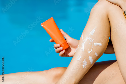 Holding sunscreen lotion tube near the legs on the blue water background. Sunscreen solar cream uv protection concept