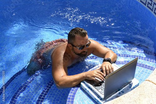 Hombre con laptop esta en la piscina disfrutando el verano